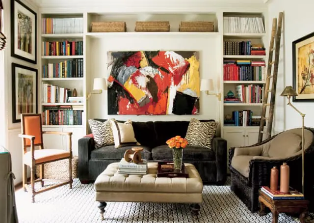Living room with dark gray sofa, tufted ottoman, built-in bookshelves filled with books, and abstract art above the sofa.
