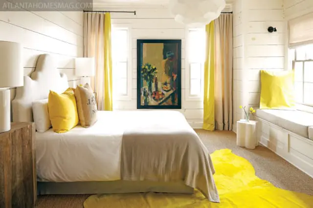 Bedroom with white shiplap walls, a king-sized bed with a scalloped headboard, yellow and beige curtains, and a large yellow rug.