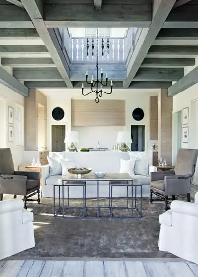Living room with white slipcovered sofa, gray armchairs, dark wood beams on ceiling, and a skylight with a black chandelier.