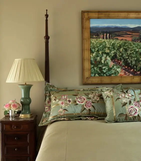 Bedroom with a dark wood four-poster bed, a green ceramic lamp on a marble-topped nightstand, and embroidered floral pillows on the bed.
