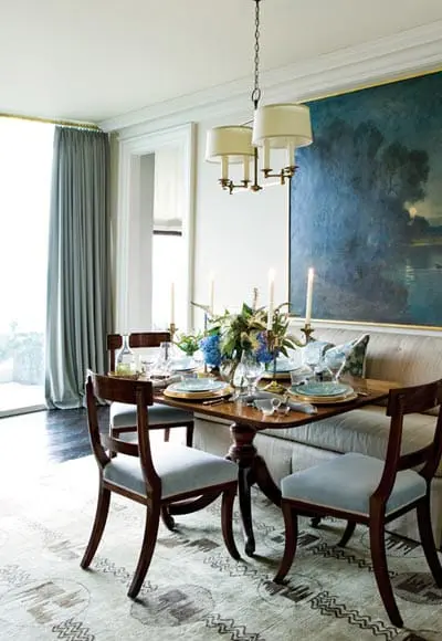 Dining room with a wooden table set for a meal, upholstered chairs, a built-in banquette, and a large abstract painting on the wall.