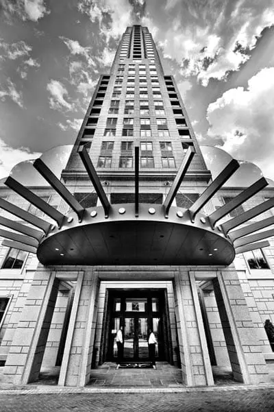 Art deco skyscraper entrance with a sunburst canopy and stone facade, viewed from below against a cloudy sky.