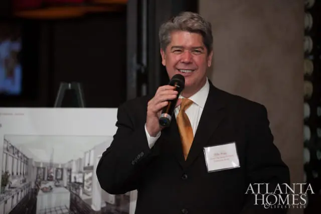Man in a black suit and orange tie holding a microphone, with a name tag that reads "Mike Briggs Atlanta Fine Homes Sotheby's International Realty"