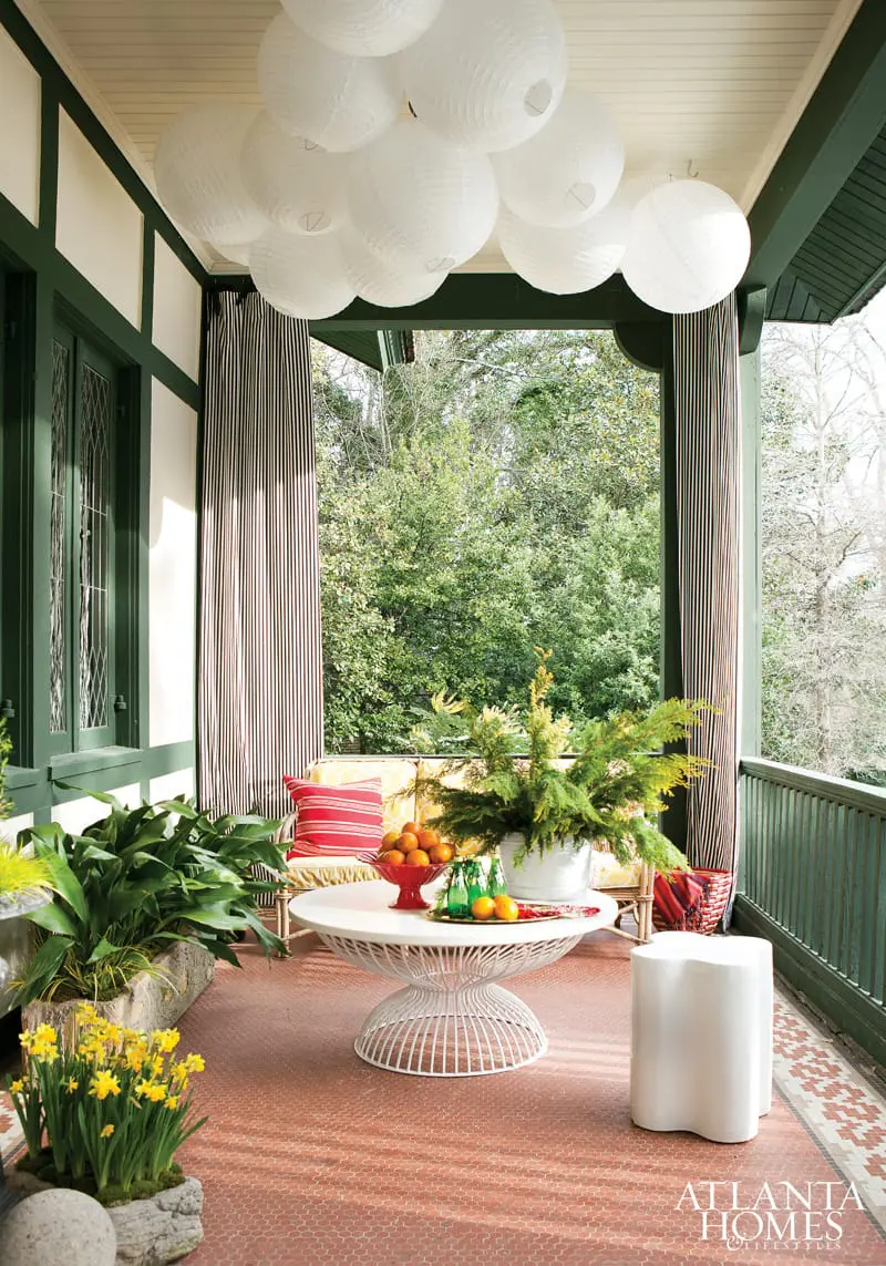 Covered porch with white paper lanterns, striped curtains, a white wire coffee table with oranges and greenery, and a white stool.