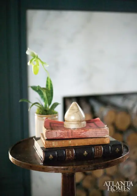 Stack of antique books on a dark wood side table with a potted orchid and a decorative finial.