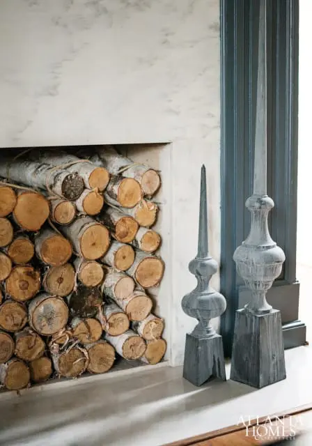 Fireplace with stacked logs and two decorative gray finials on a marble hearth. The fireplace surround is white marble with gray veining.
