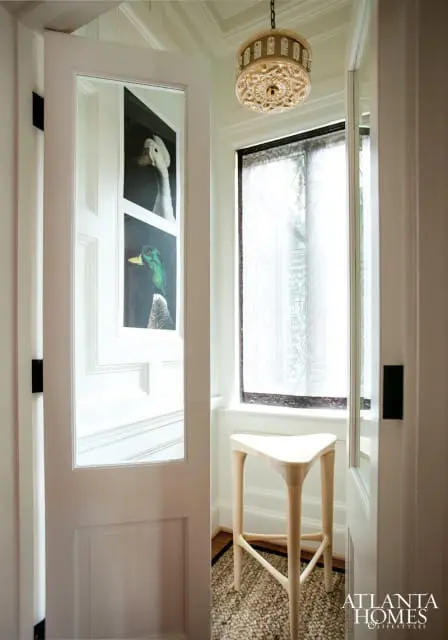 Hallway with white paneled doors featuring framed artwork of ducks, a triangular wooden stool, and a decorative chandelier