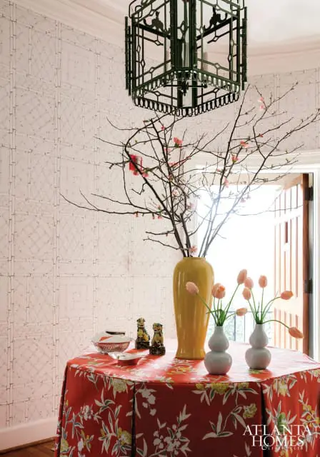 Entryway with bamboo-patterned wallpaper, a red floral tablecloth, a yellow vase with branches, and a green lantern chandelier.
