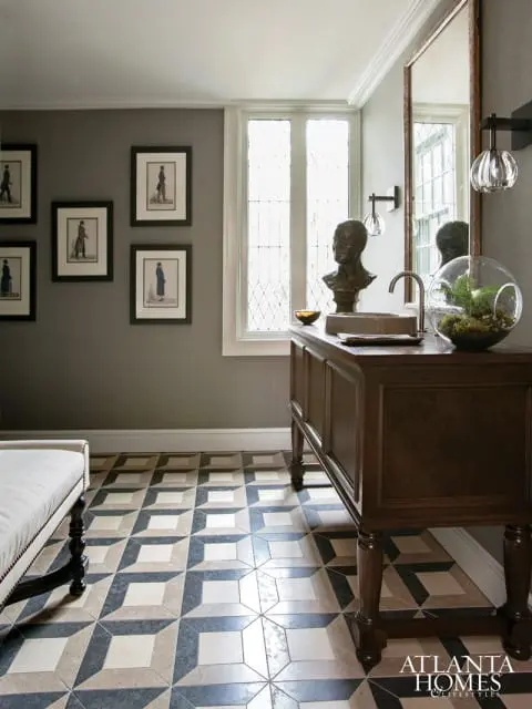 Hallway with gray textured walls, framed historical prints, a dark wood vanity with a sink and a glass terrarium, and a patterned floor with a 3D effect.