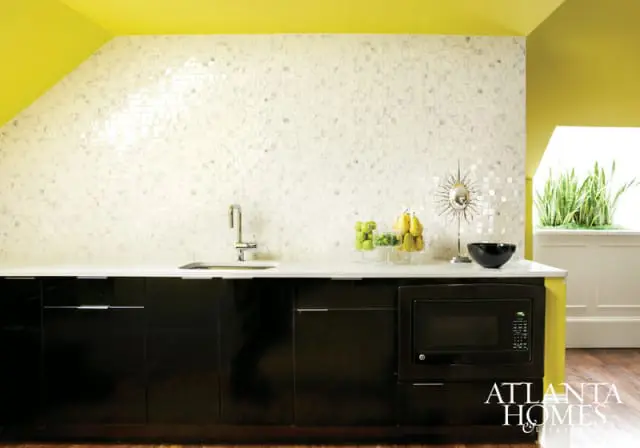 Modern kitchen with glossy black cabinets, white mosaic tile backsplash, chrome faucet, and bright yellow ceiling.