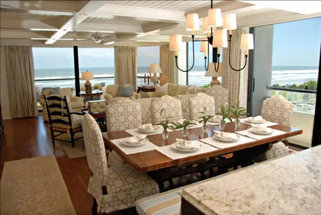 Dining room with ocean view, featuring a wooden table set for dinner, upholstered chairs with geometric pattern, and a chandelier overhead.