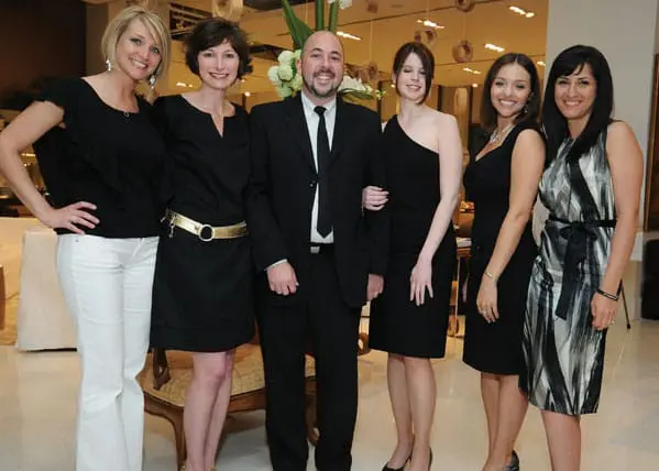 Six people, five women and one man, pose for a photo. The women wear black dresses and the man wears a black suit.