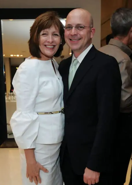Woman in white dress with puffed sleeves and man in black suit and light green tie smiling.