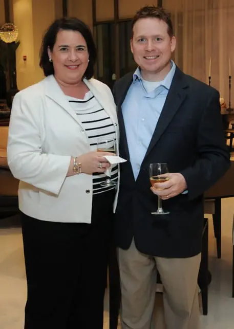 Woman in white blazer and striped top with man in navy blazer and light blue shirt, both holding wine glasses.