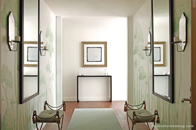 Hallway with botanical print wallpaper, two green upholstered benches with gold trim, large framed mirrors, and a console table with artwork above.