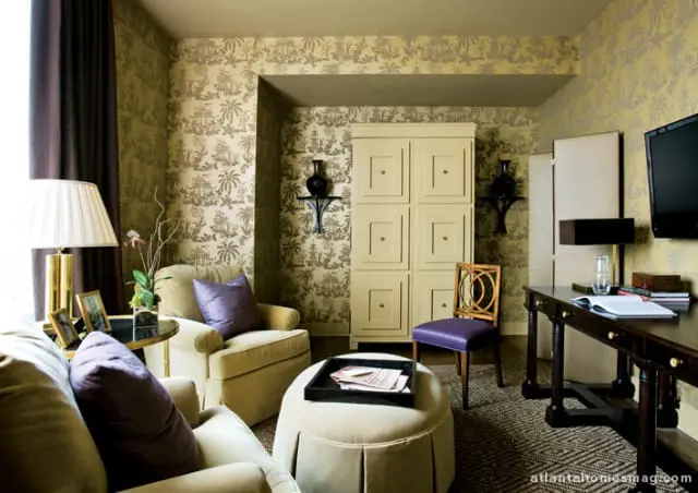 Living room with toile wallpaper, upholstered chairs, an ottoman, a desk, and a tall cabinet.