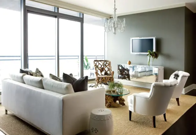 Living room with white sofa, two white armchairs, a driftwood coffee table, a mirrored credenza, and a unique carved wood chair.