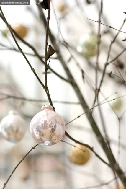 Close-up of bare branches adorned with delicate, reflective glass ornaments in muted tones of pink, gold, and silver.