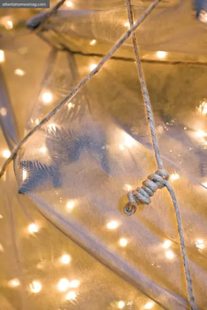 Close-up of a knot tied in jute rope against a backdrop of sheer fabric and blurred warm fairy lights.
