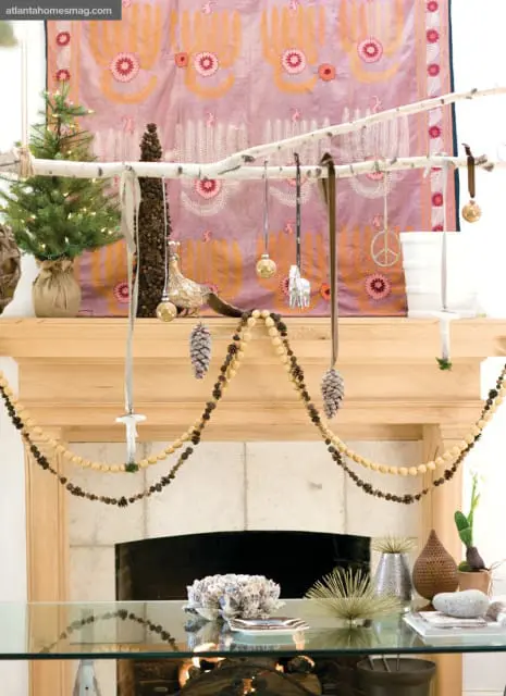 Wooden mantelpiece decorated for the holidays with a small Christmas tree, pinecone garlands, and ornaments hanging from a birch branch.