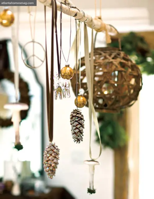 Pinecone ornaments with glitter and small gold baubles hanging from a birch branch with ribbons