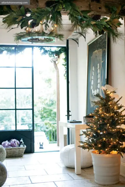 Interior entryway decorated for Christmas with a small lit tree, garland on exposed beams, and a large framed artwork on the wall.