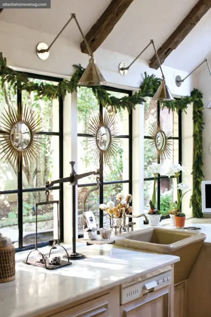 Kitchen with marble countertops, farmhouse sink, and large windows decorated with Christmas garland and sunburst mirrors.