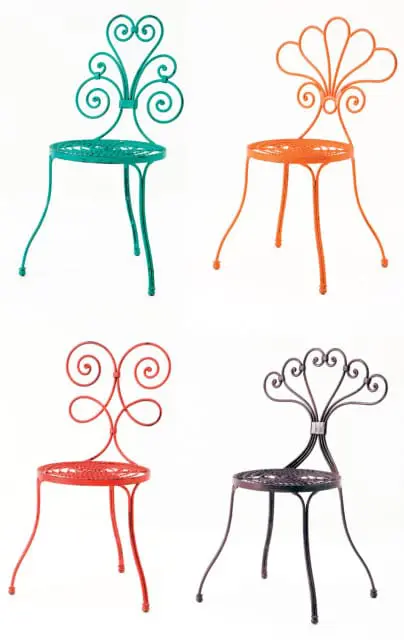 Four wrought iron chairs in teal, orange, red, and dark gray, each with decorative scrollwork on the back and a circular, perforated seat.