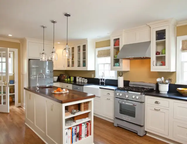 Cream kitchen with a gray retro refrigerator, a farmhouse sink, a wooden island countertop, and a gray gas range with a stainless steel hood.