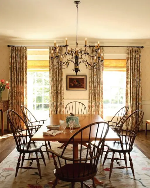 Dining room with a wooden table and chairs, a wrought iron chandelier, and floral curtains.