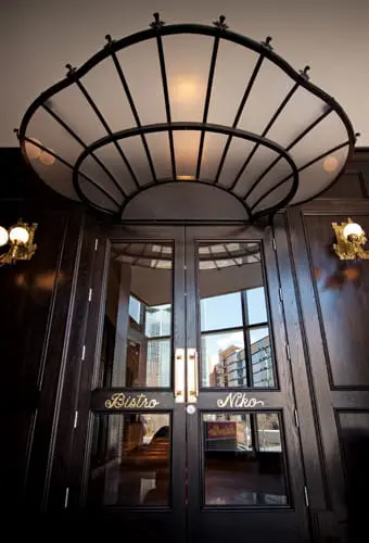 Dark wood double doors with glass panels and ornate metal awning. Gold lettering reads "Bistro Niko".