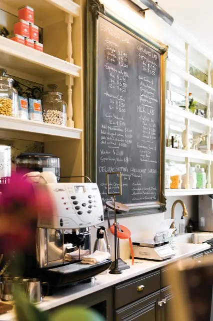 Espresso machine and chalkboard menu in a cafe. The menu lists espresso drinks, coffees, milkshakes, and chocolate services.