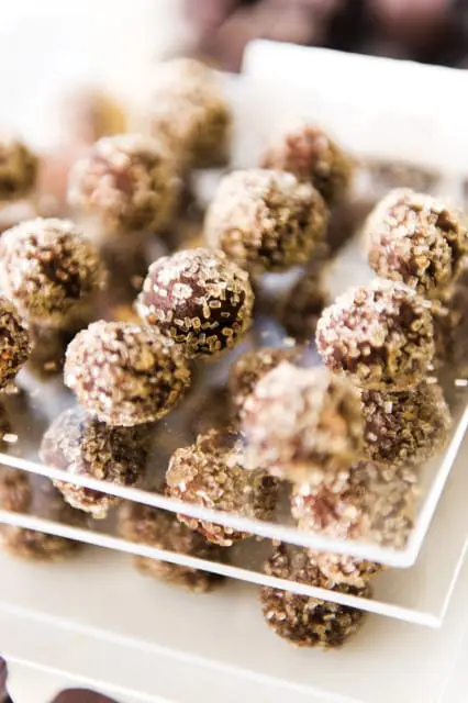 Close-up of chocolate truffles coated in coarse sugar crystals, displayed on white tiered trays.