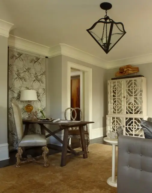 Study with a dark wood desk and ornate chairs, a patterned tapestry, a white cabinet with decorative doors, and a large textured rug.