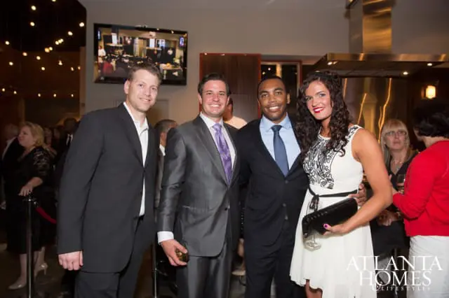 Four people posing for a photo at an event. The two men on the left are wearing suits, and the man and woman on the right are also dressed formally. A logo for Atlanta Homes & Lifestyles is visible in the lower right corner.
