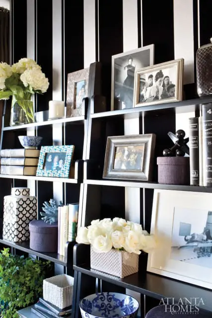 Black and white striped wallpaper behind shelves displaying framed photos, books, vases, and decorative boxes.