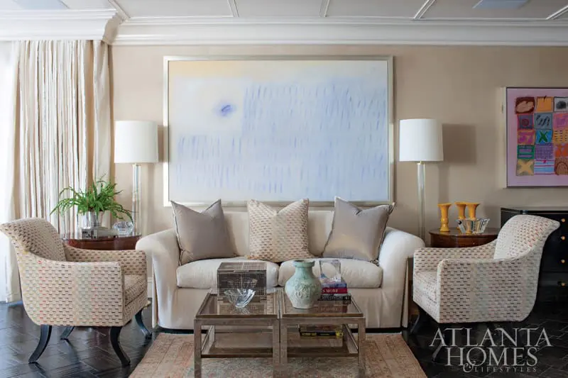 Living room with a white sofa, two patterned armchairs, a large abstract painting with blue and white tones, and a coffee table with decorative items.