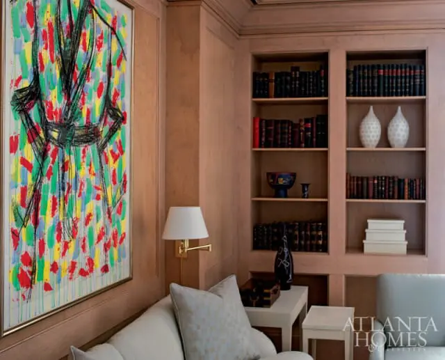 Living room with light wood paneling, built-in bookshelves filled with books, and a colorful abstract painting on the wall.