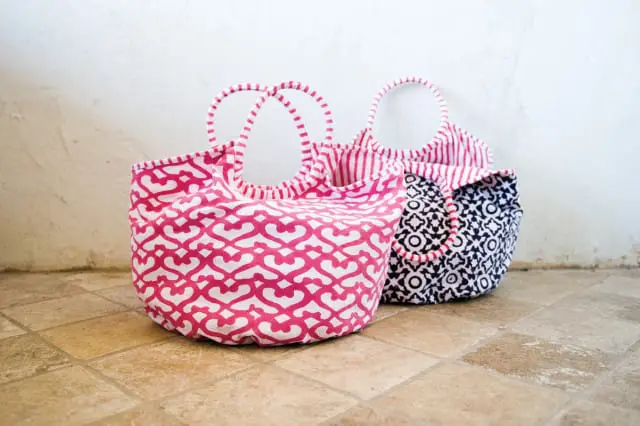 Two fabric tote bags with patterned designs: one pink with a white quatrefoil pattern, and one navy with a white geometric pattern. Both have striped handles.