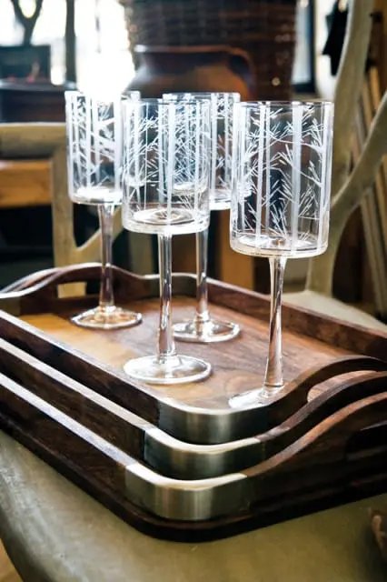 Four clear glass goblets with etched white tree branch patterns sit on a dark wood tray with metal accents.