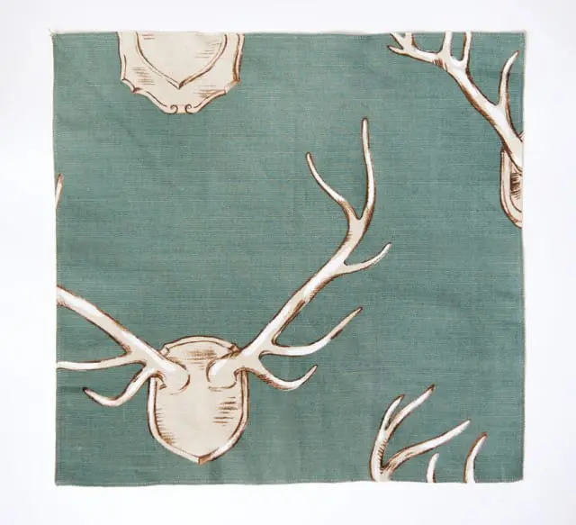 Teal fabric with a repeating pattern of sketched deer antlers mounted on shields in cream and brown