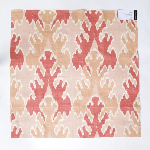 Close-up of fabric with a repeating ikat-style pattern in coral, peach, and cream on a textured linen blend.
