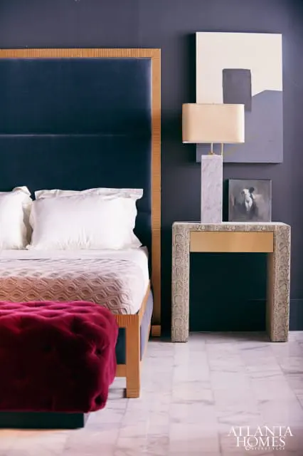 Bedroom with navy upholstered headboard, marble nightstand with gold drawer, and abstract art.