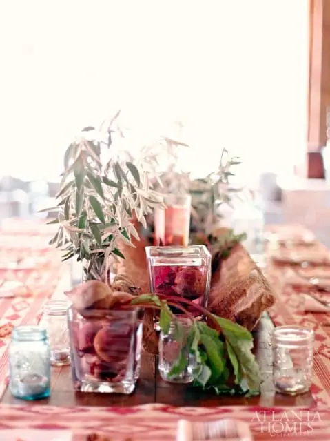 Table setting with beets in glass jars, greenery, and a rustic wooden centerpiece on a patterned runner.