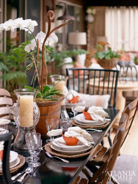For a dramatic touch, Ann Sherrill, owner of the Cashiers-based home furnishings boutqique Rusticks, employed glossy black paint on a picnic-style dining table and porch swing, both of which were made by a local craftsman, and repeated that color in the rugs underfoot. The coral hue in the fabrics tied together the dining area and sitting area, which she deliberately seperated into two distinct spaces in the outdoor space.