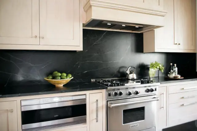 Cream kitchen cabinets above a black marble backsplash and countertop. Stainless steel range and microwave are visible.