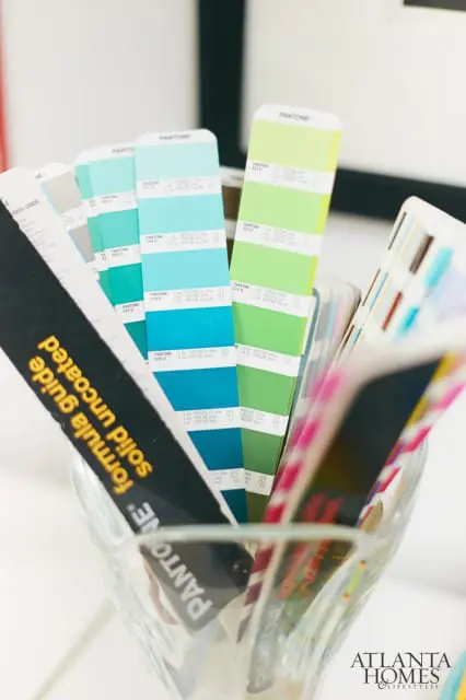 Close-up of Pantone color swatch fans in shades of blue, green, and gray, held in a glass vase. One fan displays 'Formula Guide Solid Uncoated'.