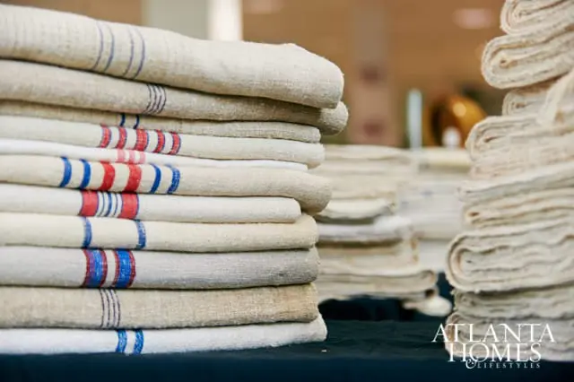 Stack of folded linen textiles with red and blue stripes, and a logo for Atlanta Homes & Lifestyles in the lower right corner.