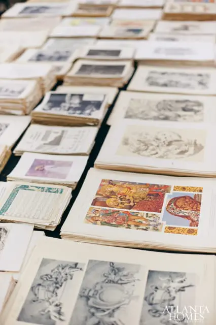 Stacks of old books and papers with illustrations and text, including a colorful depiction of figures in historical dress and black and white sketches.