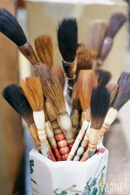 Collection of calligraphy brushes with natural bristles and carved wooden handles in a decorative ceramic container with painted figures